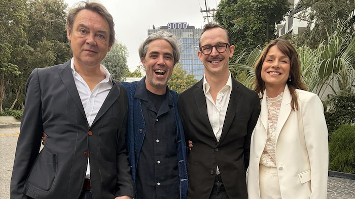Trois hommes et une femme posent. 