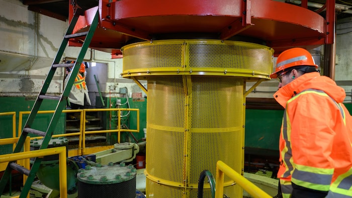 Une turbine qui tourne rapidement. Un homme porte un casque de protection tout près.