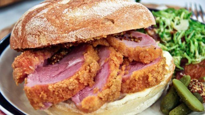 Un sándwich de tocino reposa en un plato junto con una ensalada. 