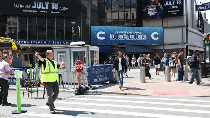 Des personnes marchent à coté du madison square garden et quelqu'un dirige la circulation.