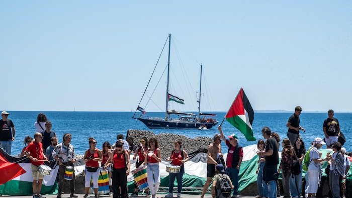 Un groupe d'hommes et de femmes sur un quai avec un voilier en arrière-plan.