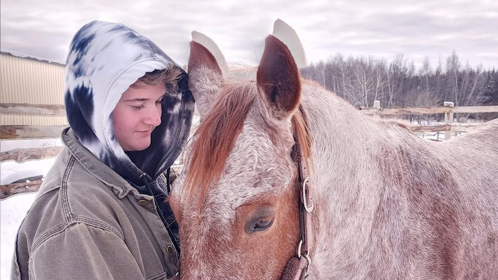 Un jeune avec un chandail à capuchon et un cheval à l'extérieur en hiver