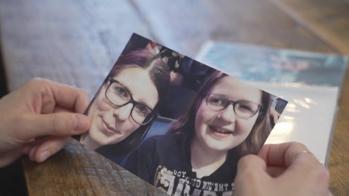 Gros plan sur une photographie tenue par deux mains sur une table en bois. La photo montre un gros plan de deux personnes.
