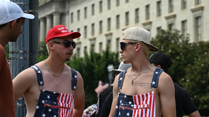 Deux jeunes hommes sont vêtus de drapeaux américains. L'un porte une casquette au slogan « Make America Great Again ».
