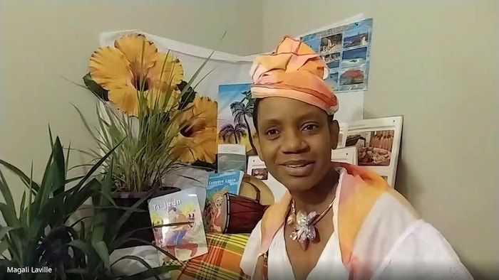 Magali Laville assise devant une table sur laquelle sont disposés des fleurs, des peintures et des livres.