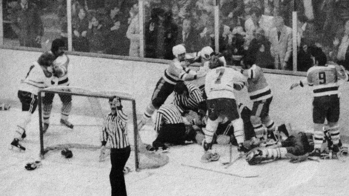 Des joueurs de hockey se bagarrent derrière la zone des buts.