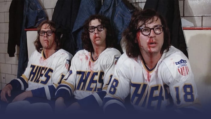 Une photo de trois joueurs de hockey assis côte à côte, le nez en sang. L'image est tirée du film Slap Shot.