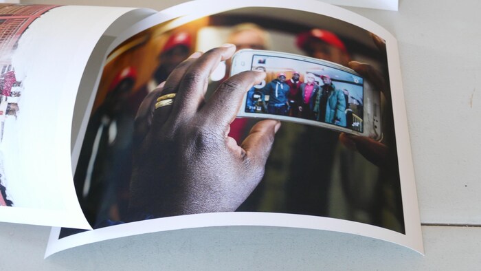 Une main tient un cellulaire qui montre une photo de groupe de 3 hommes noirs et 1 homme blanc. 