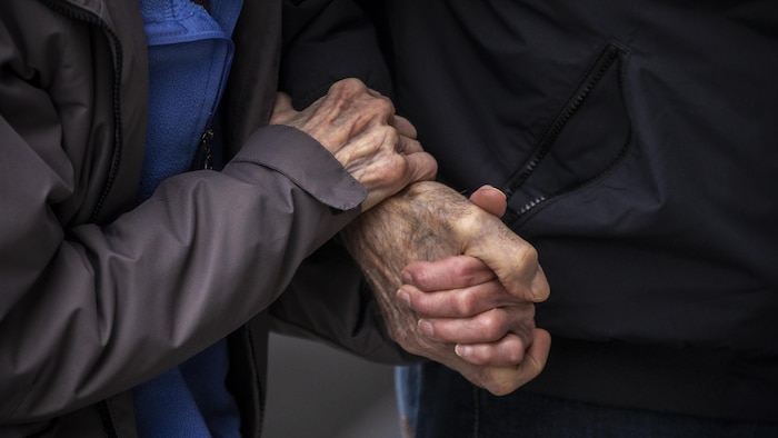 Une paire de mains d’une personne âgée s'agrippent à une autre main.