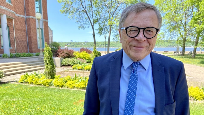 Gilles Lehouillier sur les terrains de l’hôtel de ville de Lévis lors d’une journée ensoleillée de printemps. Il sourit à la caméra. À l’arrière-plan, on distingue le fleuve Saint-Laurent et la Rive-Nord.