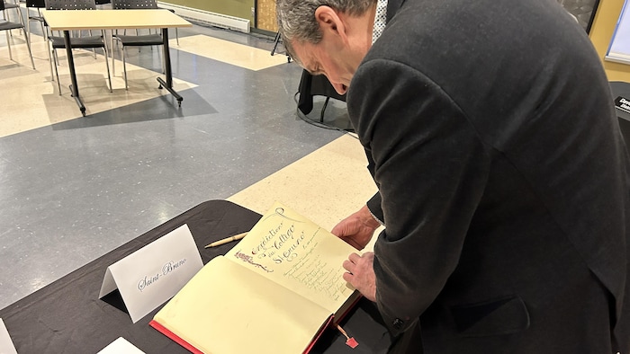 Un maire lit un livre d'or sur une table.