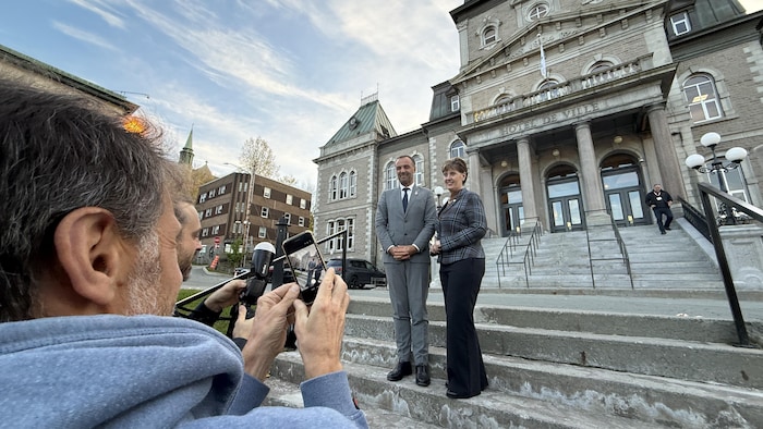 La mairesse de Sherbrooke, Marie-Claude Bibeau, et le maire de Montpellier, Michaël Delafosse, devant l'hôtel de ville de Sherbrooke, se font photographier par les médias.