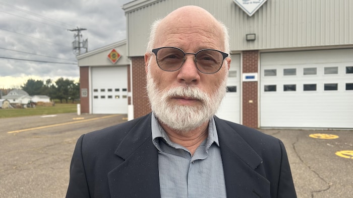Un homme sourit à la caméra, devant un garage municipal.