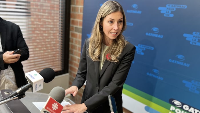 Une femme aux cheveux longs et blonds devant un podium avec des micros.
