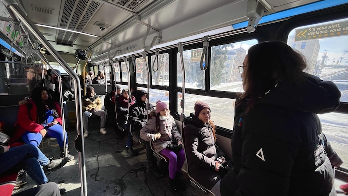 La mairesse se tient debout dans un autobus de Société de transport de Sherbrooke. Devant elle, des nouveaux arrivants sont assis sur des sièges.