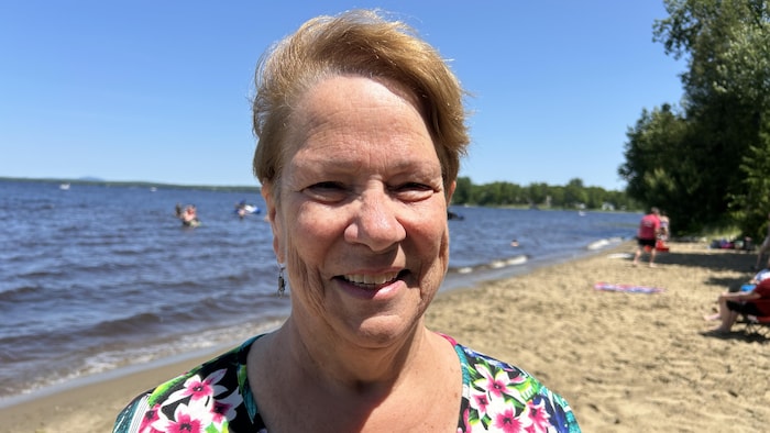 La mairesse sourit, debout sur la plage, vêtue d'un chandail fleuri.