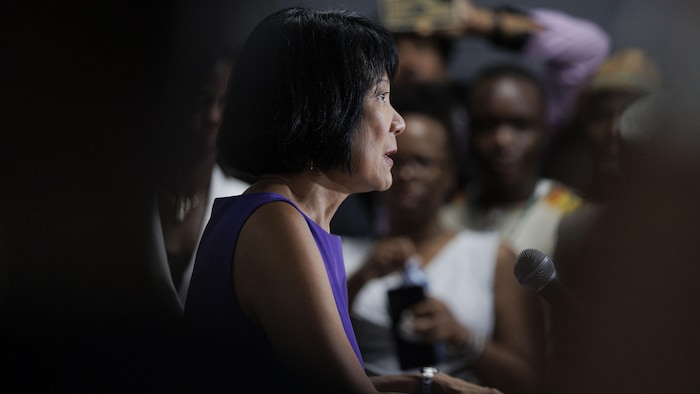 Olivia Chow devant un podium, vue de côté, avec des demandeurs d'asile à l'arrière.
