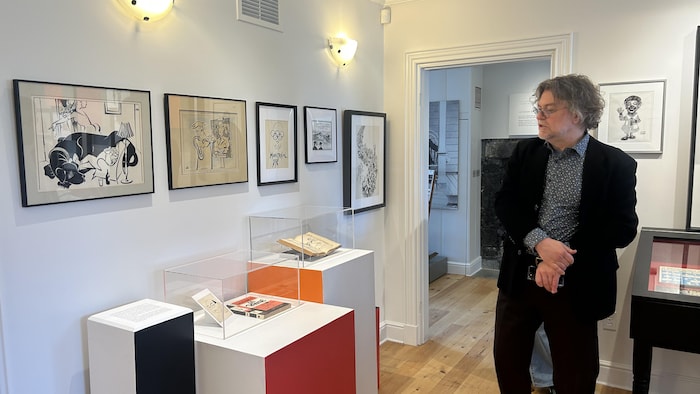 Une personne regarde des livres et des dessins présentés dans une salle d'exposition du Centre d’interprétation historique de Sainte-Foy.