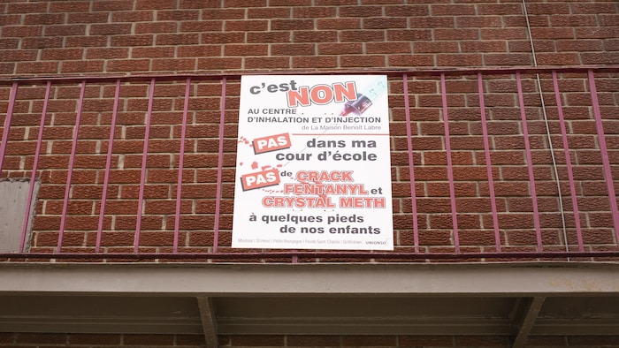 Une affiche protestant contre le centre de consommation supervisée est visible sur un bâtiment.