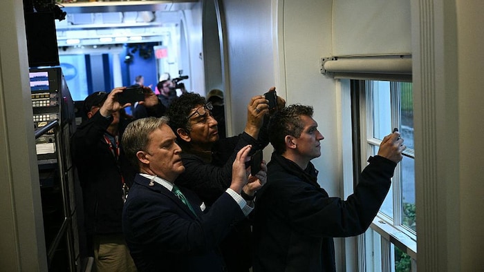 Des journalistes brandissent leurs téléphones et filment des fenêtres une action qui se passe à l'extérieur.
