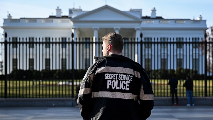 Un agent qui porte un manteau des services secrets est debout devant la Maison-Blanche.