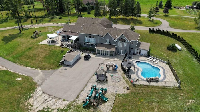 Sa grande maison vue des airs, avec une piscine creusée, un trampoline et un parc pour enfants.