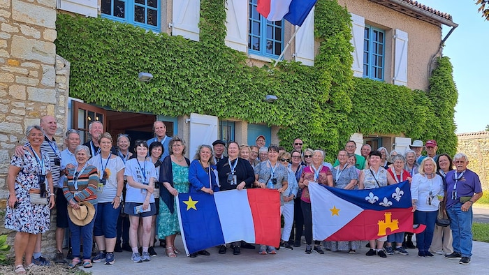 Un groupe d'une trentaine de personnes pose à l'extérieur pour une photo. Ils tiennent un drapeau acadien et un drapeau cajun devant eux.