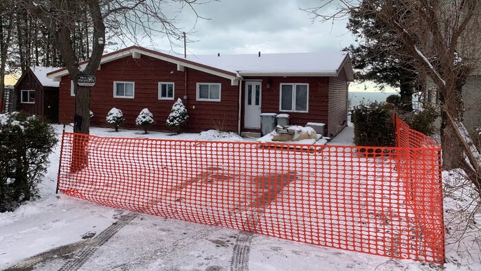 Une clôture de plastique barre l'accès à l'entrée de la maison, derrière laquelle on aperçoit les eaux du lac Huron.