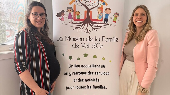Deux femmes posent pour la photo, au milieu d’une large pancarte sur laquelle est écrit la maison de la famille de Val-d’Or.