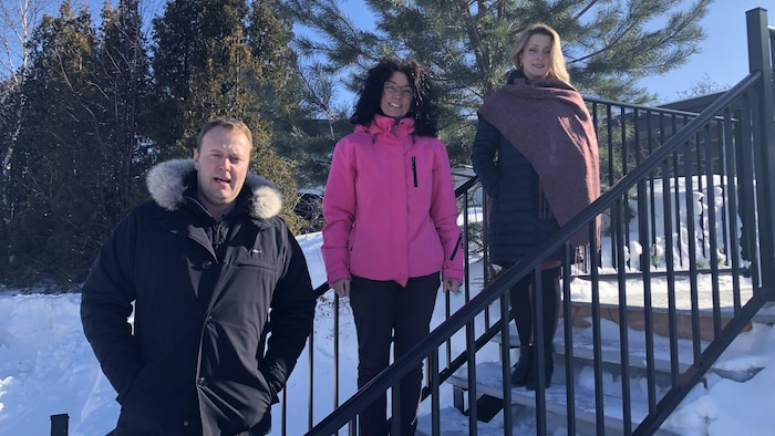 Un homme et deux femmes posent dans des marches dehors l'hiver.