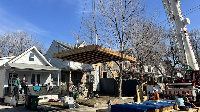 Un panneau préfabriqué est soulevé par une grue devant la maison de la famille Page-Kern.
