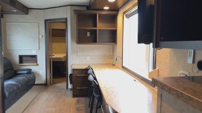 L'intérieur étroit d'une caravane meublée qui comprend un fauteuil, des chaises, un bureau et des étagères. 