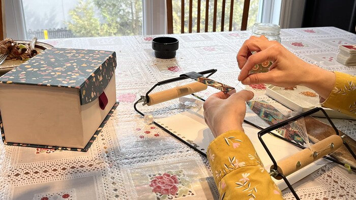 Une femme anonyme confectionne un bijou avec des billes, du fil et une aiguille. 