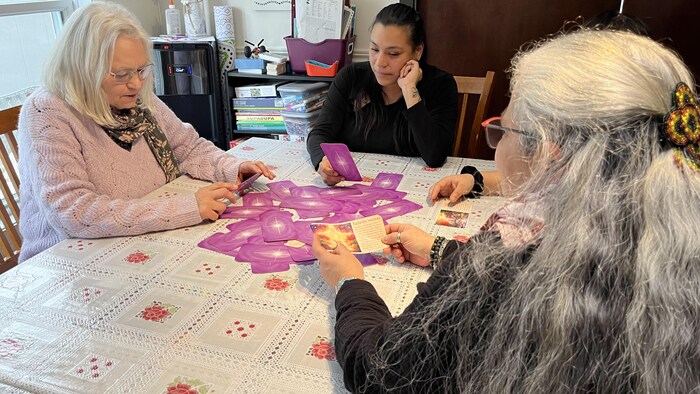 Trois femmes sont assises autour d'une table et lisent des cartes sur la croissance personnelle. 