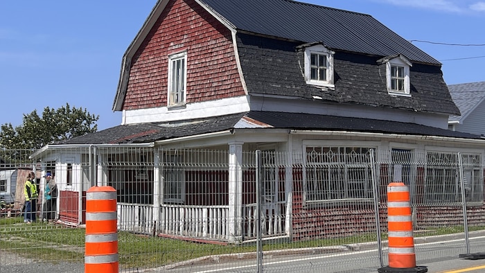 La maison Potvin, entourée de grillage, avec devant des cônes orange.