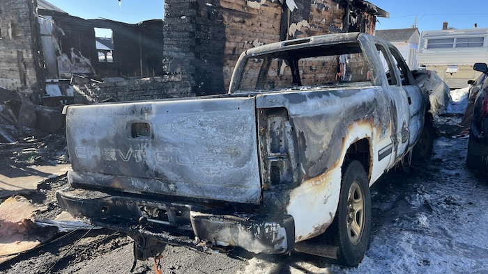 Une voiture calcinée est stationnée à côté d'une maison ravagée par un incendie. 