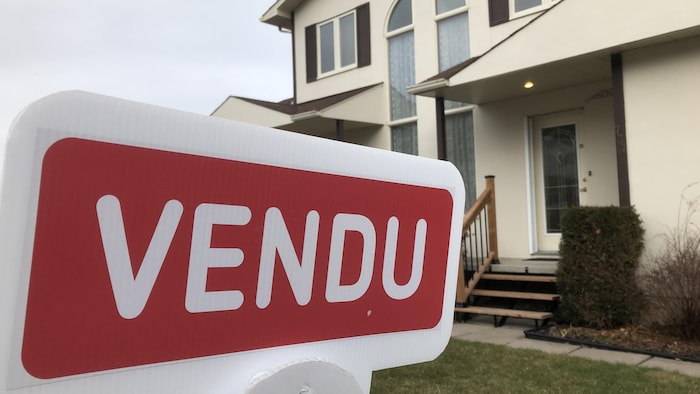 Une pancarte de maison vendue, devant une maison.