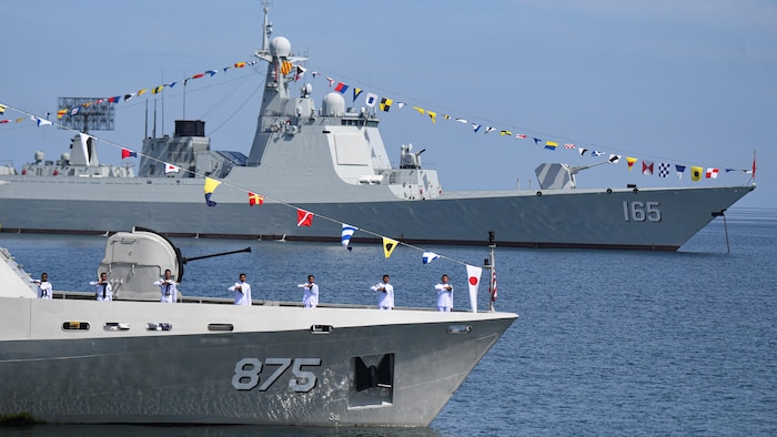 Des militaires sont debout sur un navire militaire, avec à l'arrière-plan un autre bateau militaire.