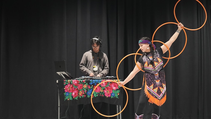 Makhena danse avec 5 cerceaux avec son frère, en arrière-plan.