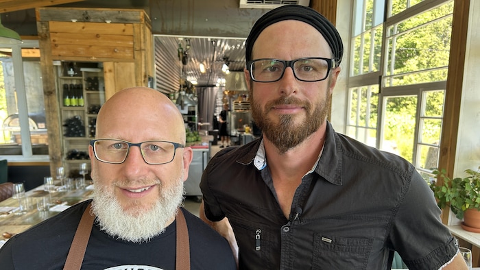 Les deux hommes sont dans le restaurant et sourient à la caméra.