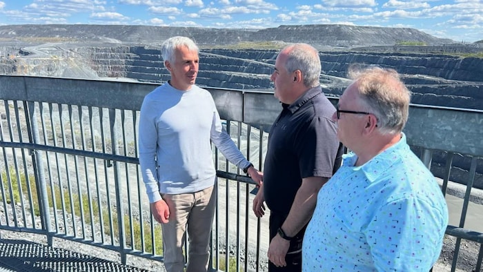 Trois hommes discutent devant une mine à ciel ouvert.