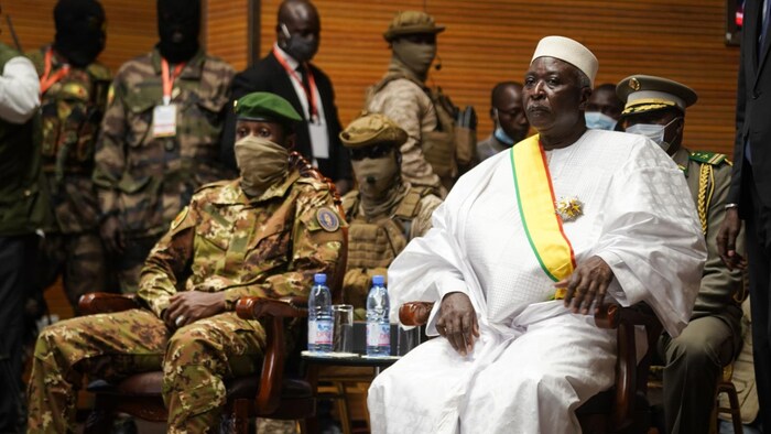 Le président, vêtu en blanc, est assis à côté du vice-président, en treillis militaire. Plusieurs militaires en uniforme sont derrière eux. 