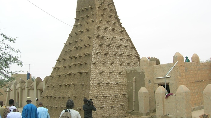 Un groupe des personnes contemplent un bâtiment en brique avec un minaret assortit des morceaux des bois.