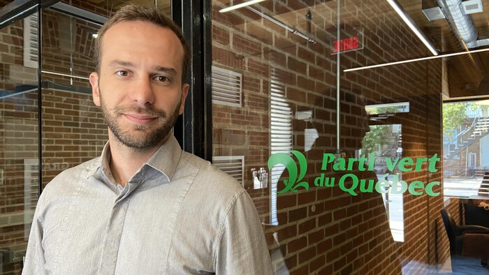 Un homme devant une porte en verre sur laquelle est écrit "Parti vert du Québec".