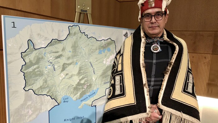 Le chef élu John Powell de la Première Nation Mamalilikulla devant la carte de la nouvelle aire protégée et de conservation autochtone.