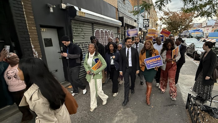 Zohran Mamdani marche en compagnie de ses partisans sur le trottoir. 