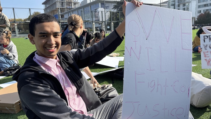 Un jeune étudiant tient une pancarte.