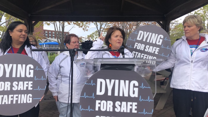 Quatre femmes sous un gazebo avec des pancartes sur lesquelles sont écrits les mots : Dying for Safe Staffing.
