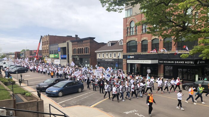 Une longue procession de centaines de personnes vêtues de blousons blancs défile dans une rue en agitant des drapeaux et des pancartes. 