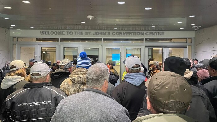 Des gens, en grande majorité des hommes, sont debout, de dos, face aux portes du centre des congrès.